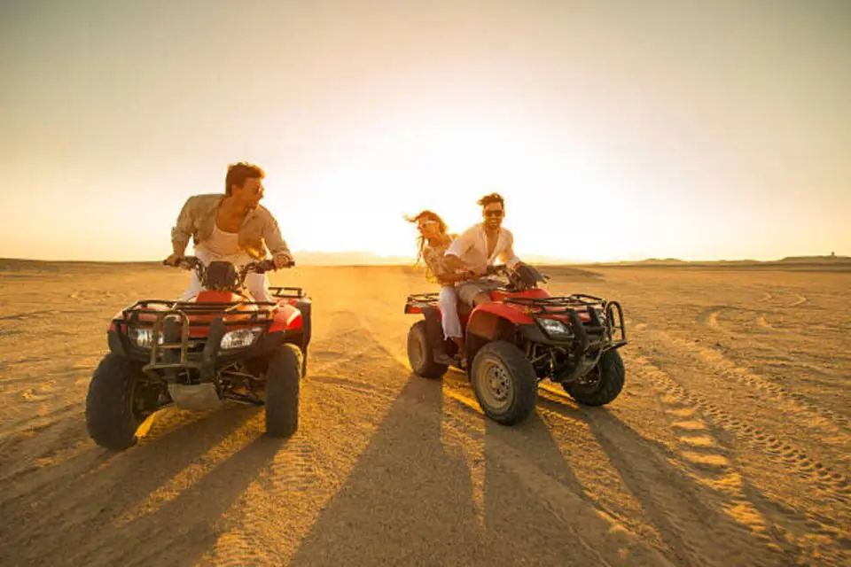 Three friends riding quad bikes across the desert at sunset