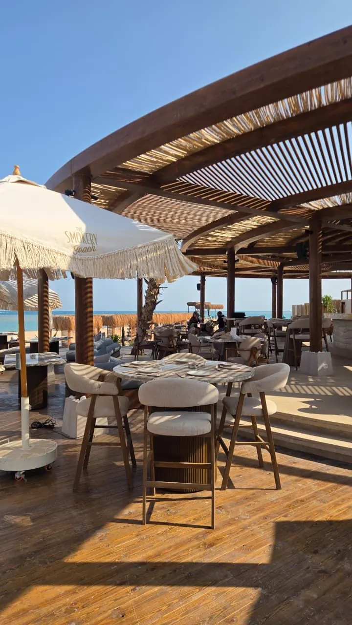 High tables under the slatted roof at The Smokery Beach with the sea behind