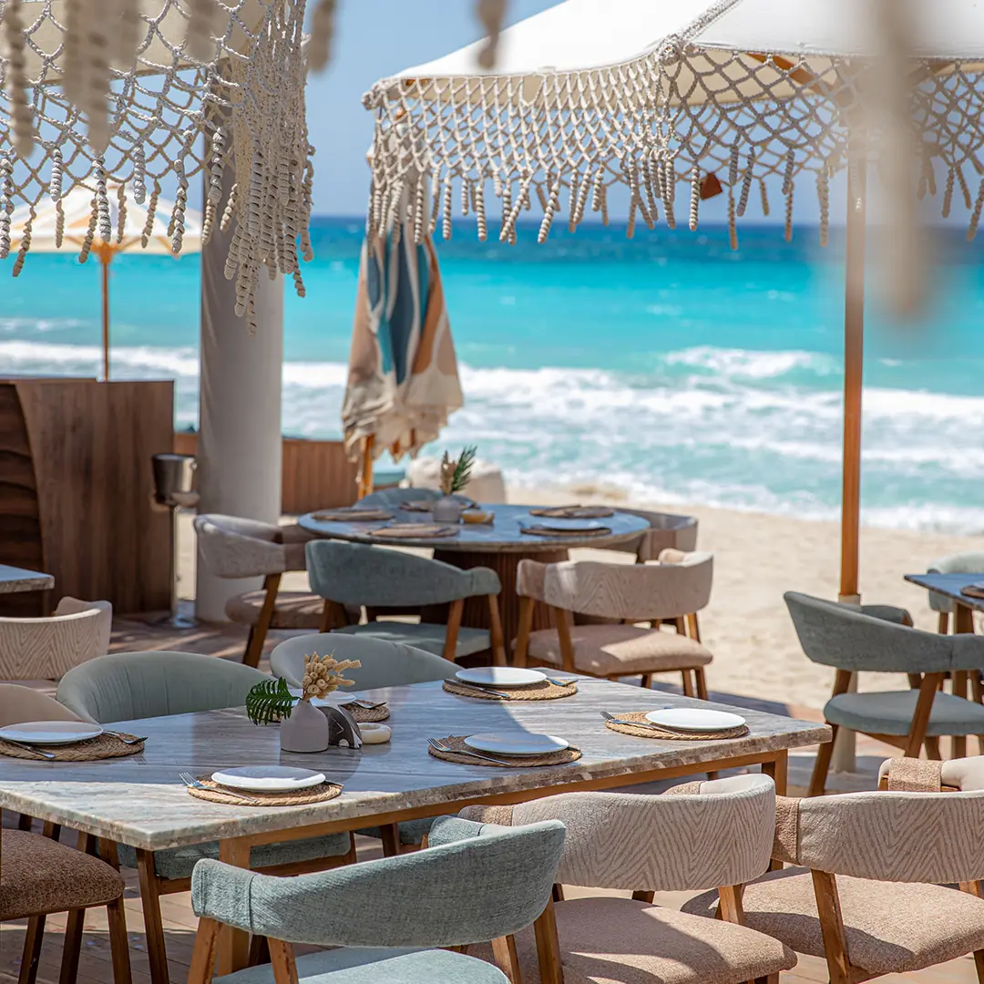 Beach dining setup with parasols and turquoise water behind